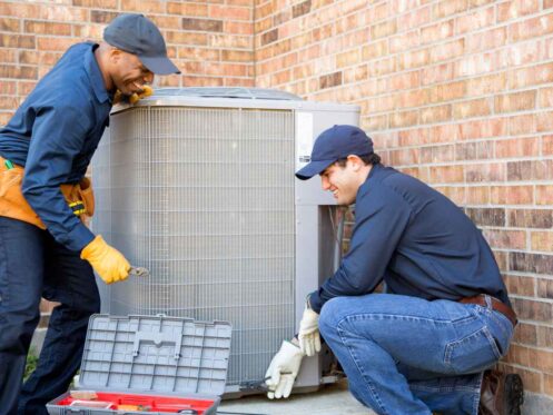 Two HVAC technicians performing maintenance on an AC system outside of a residential home.