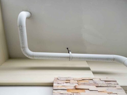 The white curve pipe for drainage of the air conditioner system is hanging on the ceiling of the office building, below the view with the copy space.