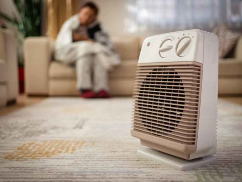 Person heating their hands at home over a domestic portable radiator in winter, energy crisis