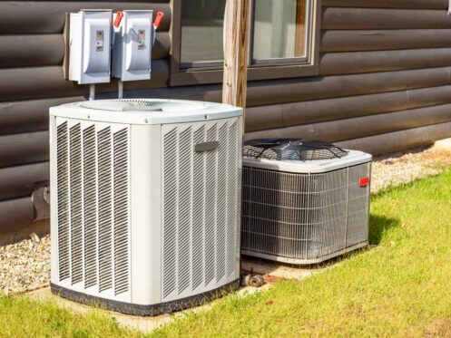 Heating and air conditioning system external units on grass in a house backyard.