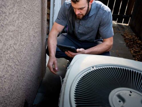 Male HVAC technician working on an AC unit outside of a home