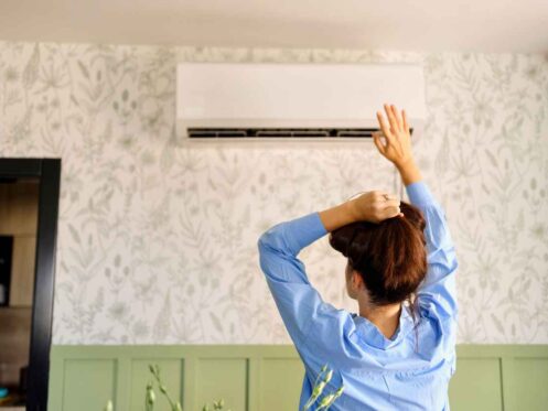 A woman lifting her hair up in front of her air conditioner because it is not blowing cold air