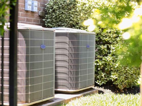 Air conditioner unit outdoors in side yard of a brick home in hot summer season.