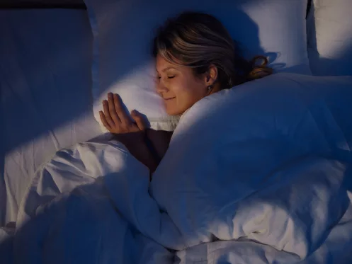 High angle view of young woman smiling while dreaming in bed at night.