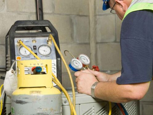 A service technician is using gauges a recovery pump and tank to remove refrigerant from a residential air conditioning system in preparation for servicing.